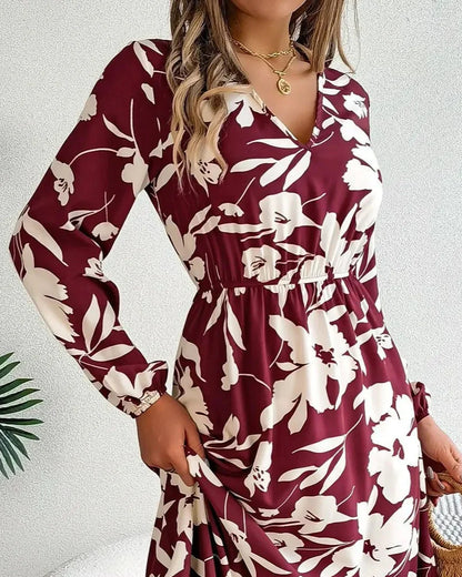 Woman wearing a burgundy and white floral dress holding a straw bag indoors.